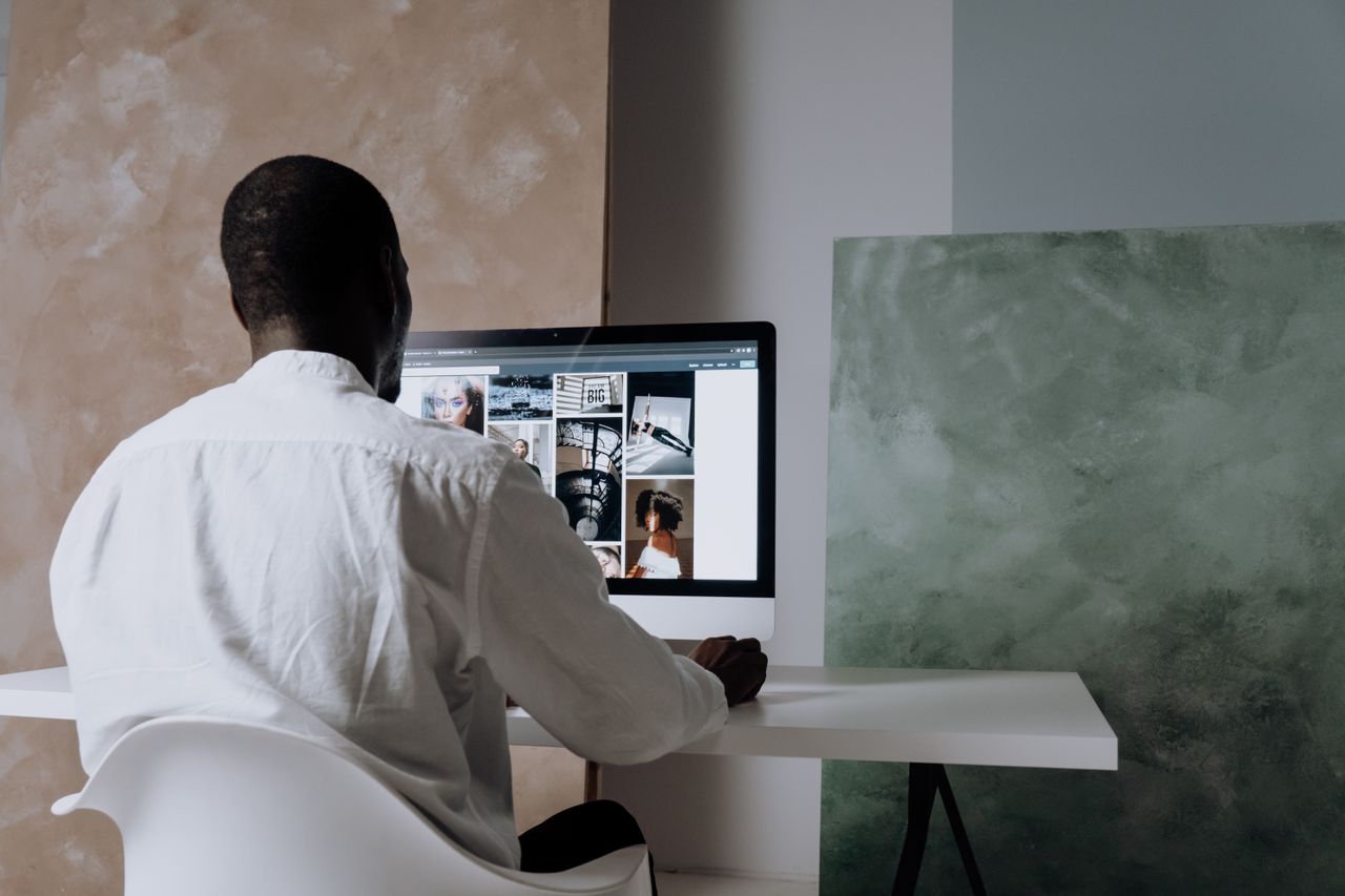 Home Back view of a man sitting at a computer, browsing images in a modern workspace.